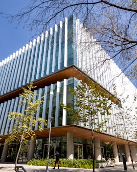 Contemporary glass-fronted office building with trees in urban setting on a sunny day.